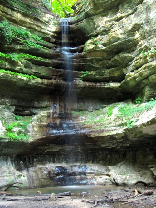 A serene waterfall cascading down rocky cliffs, surrounded by lush greenery and a small pool at the base.