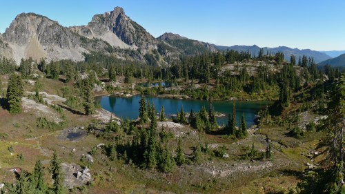 A scenic landscape featuring a tranquil lake surrounded by mountains and lush greenery under a clear blue sky.