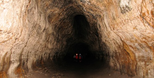 A dark cave interior with textured rock walls and small figures of people in the distance.