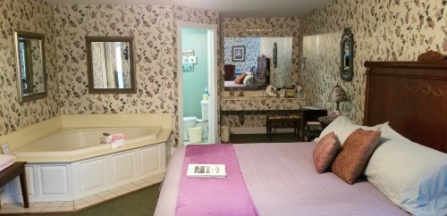 Cozy bedroom with floral wallpaper, a large bed, a jacuzzi tub, and a mirrored vanity area.