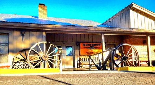 A rustic building with large wooden wagon wheels displayed outside, under a clear blue sky.
