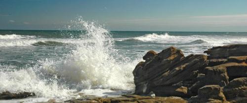 Waves crashing against rocky shore under a clear blue sky.