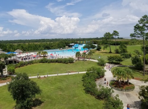 Aerial view of a large swimming pool surrounded by greenery and people enjoying a sunny day.