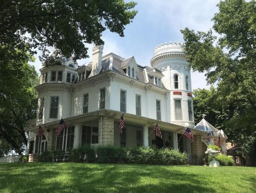 A grand, historic mansion with a turret, surrounded by trees and adorned with American flags.