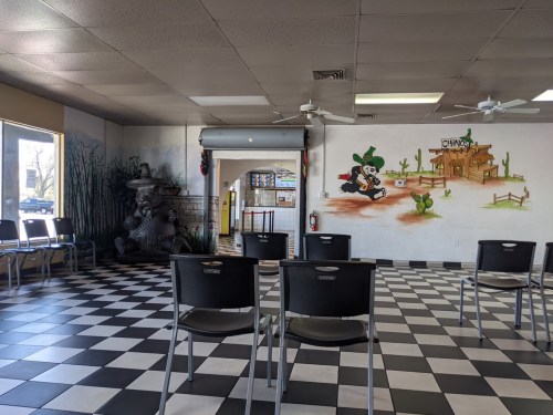 Interior of a restaurant with black and white checkered floor, empty chairs, and a mural of a cartoon character.