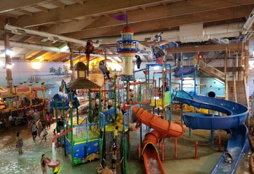 A vibrant indoor water park featuring colorful slides, play structures, and families enjoying the water.