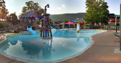 A serene water park scene featuring a shallow pool, water slides, and lush greenery in the background.