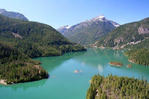 A serene mountain landscape featuring a turquoise lake surrounded by lush green forests and towering peaks.