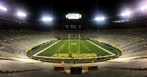 A wide view of a darkened football stadium with empty seats and a well-lit field marked "Green Bay."
