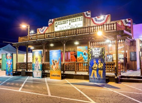 A wooden theater building with a sign reading "Gaslight Theatre," decorated with banners and colorful posters outside.