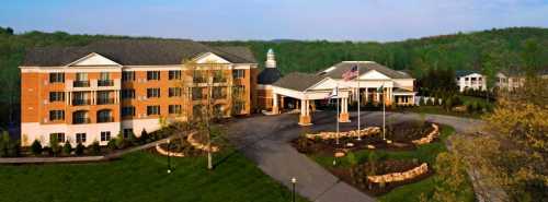 A large hotel building with a landscaped entrance, surrounded by greenery and a clear blue sky.