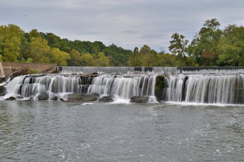 A serene waterfall cascading over rocks, surrounded by lush green trees under a cloudy sky.