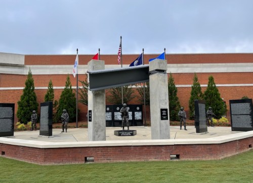 A memorial featuring statues of soldiers, flags, and engraved stone panels, set in a landscaped area.