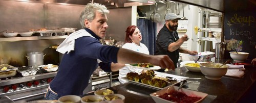 A busy kitchen scene with three chefs preparing and plating dishes, surrounded by pots and pans.