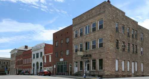 Historic buildings line a street under a clear blue sky, showcasing a mix of architectural styles.