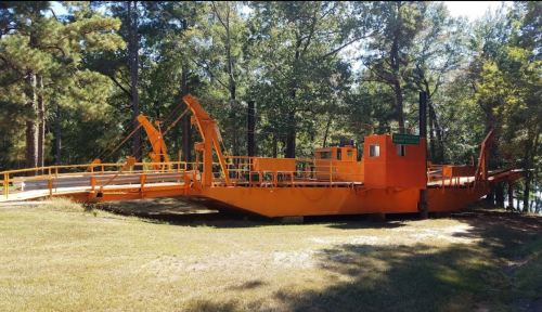 An orange flatboat with ramps, surrounded by trees and grass, near a body of water.
