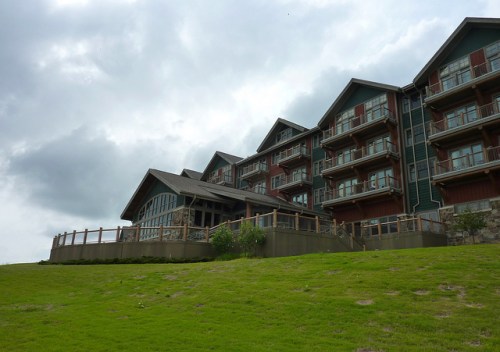 A large, multi-story lodge with balconies, set against a cloudy sky and green grassy landscape.