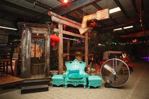 A vibrant indoor space featuring a turquoise chair, decorative lanterns, and a large illuminated arrow sign.