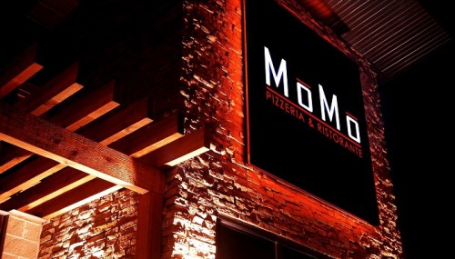 Illuminated sign for MoMo Pizzeria & Ristorante on a brick wall at night.