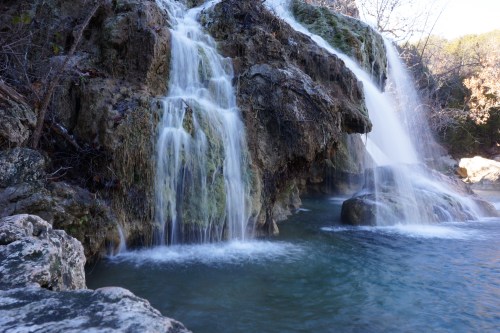 A serene waterfall cascading over rocky terrain into a clear pool, surrounded by lush greenery.