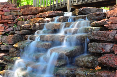 A serene waterfall cascading over smooth, stacked stones, with a wooden bridge in the background.