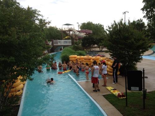 A group of people at a water park near a lazy river and inflatable tubes, with a water slide in the background.