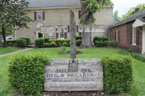 Sign for Jailer’s Inn Bed & Breakfast in front of a stone building, surrounded by green grass and trees.