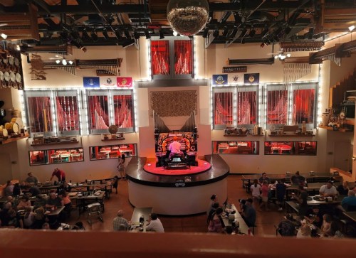 A lively restaurant interior with a stage featuring a performer on an organ, surrounded by diners and vibrant decor.