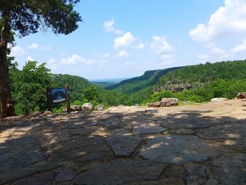 A scenic view of lush green hills and valleys under a blue sky with fluffy clouds, featuring a stone pathway in the foreground.