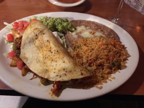 A plate of Mexican food featuring a quesadilla, rice, refried beans, guacamole, and diced tomatoes.