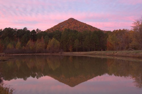A serene lake reflects a colorful sunset over a mountain surrounded by autumn trees.