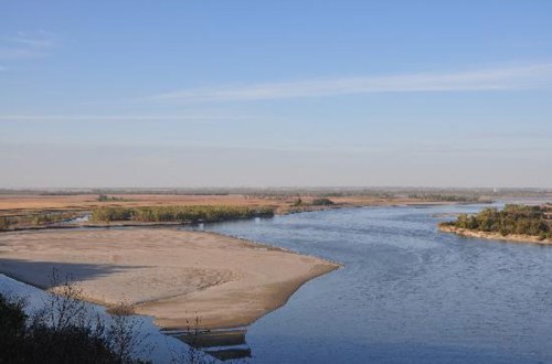 A serene river landscape with sandy banks and lush greenery under a clear blue sky.