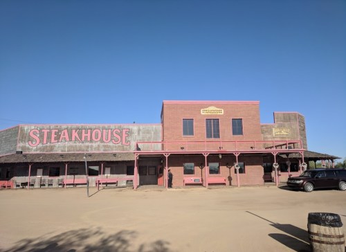 A rustic steakhouse building with a pink facade and wooden accents, set against a clear blue sky.