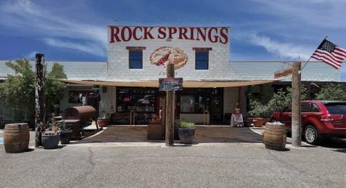 A rustic building with "Rock Springs" sign, featuring an American flag, barrels, and a welcoming entrance.