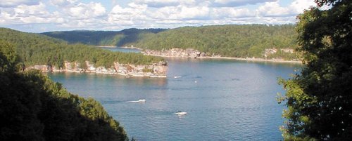A serene lake surrounded by lush green forests and rocky cliffs under a partly cloudy sky.