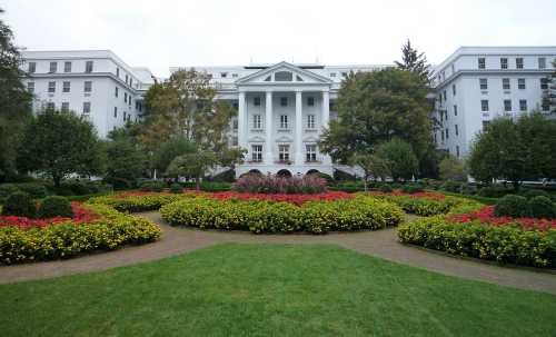 A grand white building surrounded by colorful flower beds and lush greenery in a landscaped garden.