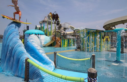 A colorful water park featuring a surfboard statue, water slides, and playful water features.