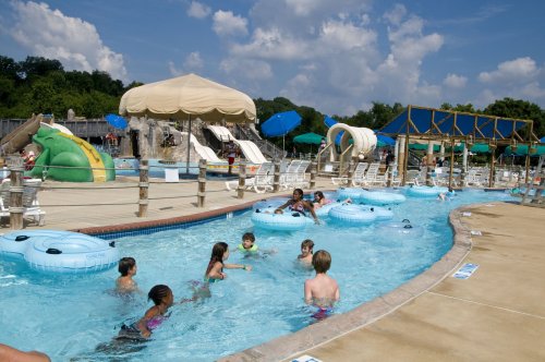 A lively pool scene with children playing, water slides, and lounge chairs under sunny skies.