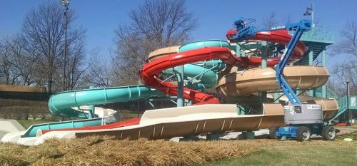 A colorful water slide structure with multiple twisting slides, surrounded by bare trees and a blue sky.