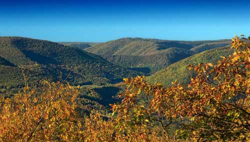 A scenic view of rolling hills covered in autumn foliage under a clear blue sky.