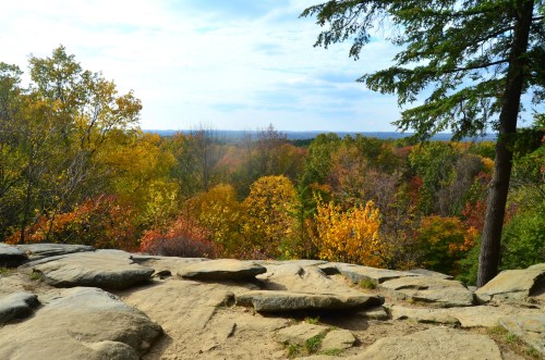 A rocky overlook with vibrant autumn foliage in the background under a partly cloudy sky.