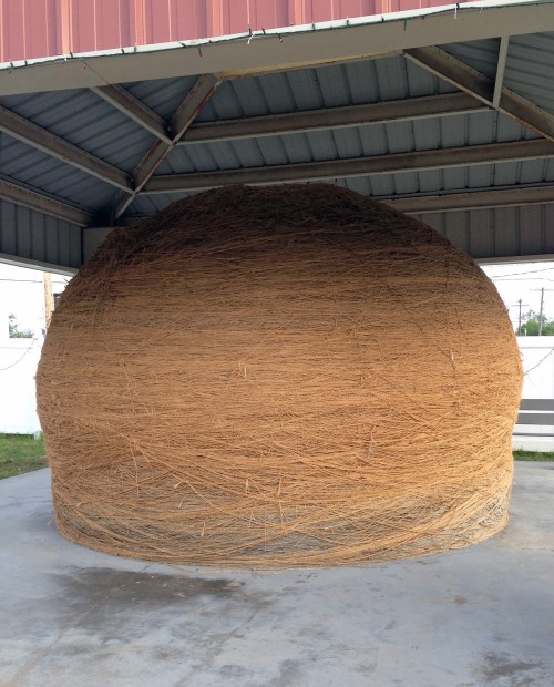A large, round structure made of tightly bundled straw, under a metal roof in a shaded area.