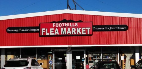 Sign for "Foothills Flea Market" on a red building, with cars parked in front and various items visible in the windows.