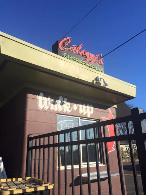 A colorful sign for "Calagione's Cheesesteaks" on a building with a clear blue sky in the background.