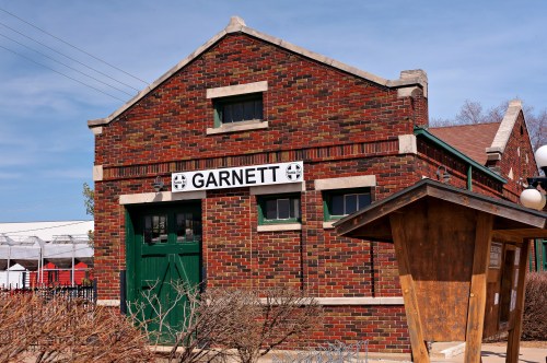 Historic brick building with a sign reading "Garnett," featuring green doors and windows against a clear blue sky.