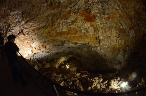 A dimly lit cave with rocky walls and a person standing near a railing, observing the interior.