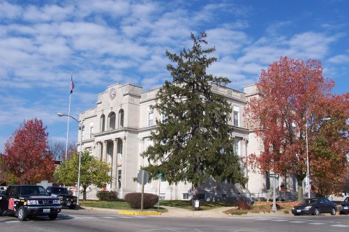 A historic building with a flag, surrounded by colorful autumn trees and parked cars under a blue sky.