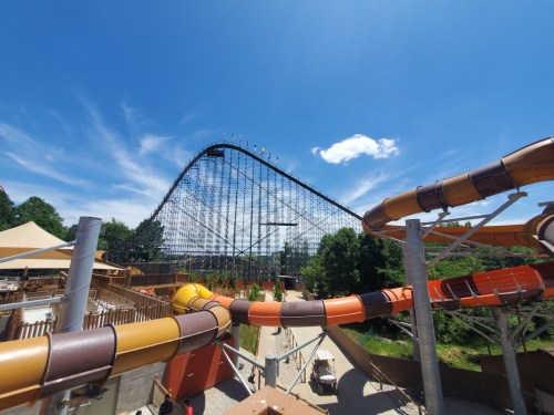 A tall roller coaster looms against a blue sky, with colorful water slides in the foreground.