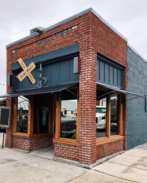 A brick building with large windows and a sign reading "Train Wreck Grill," featuring a rustic, inviting exterior.