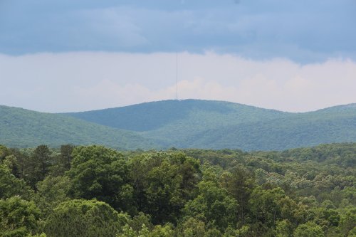 A panoramic view of green mountains under a cloudy sky, with a tall tower visible in the distance.